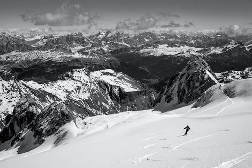 Černobílá fotografie: Lyžař v Italských Alpách. Zasněžené hory a oblaky. Lyžařské středisko.