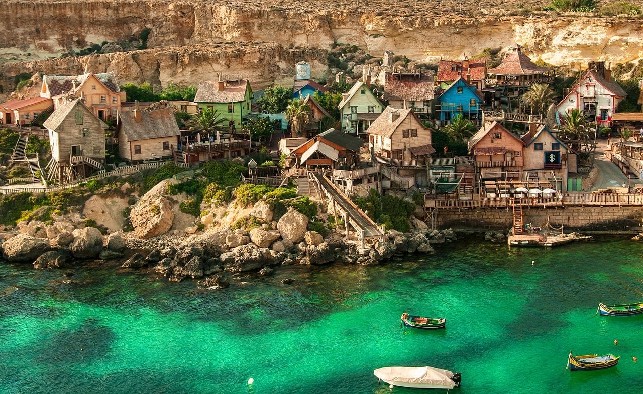 Malta, Popeye Village. Barevné domy u moře, lodě na tyrkysové vodě. Turistická destinace.