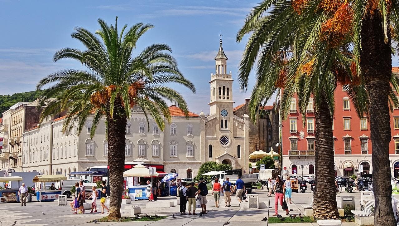 Split, Chorvatsko: Náměstí s palmami, kostel a lidé. Letní dovolená v Dalmácii.