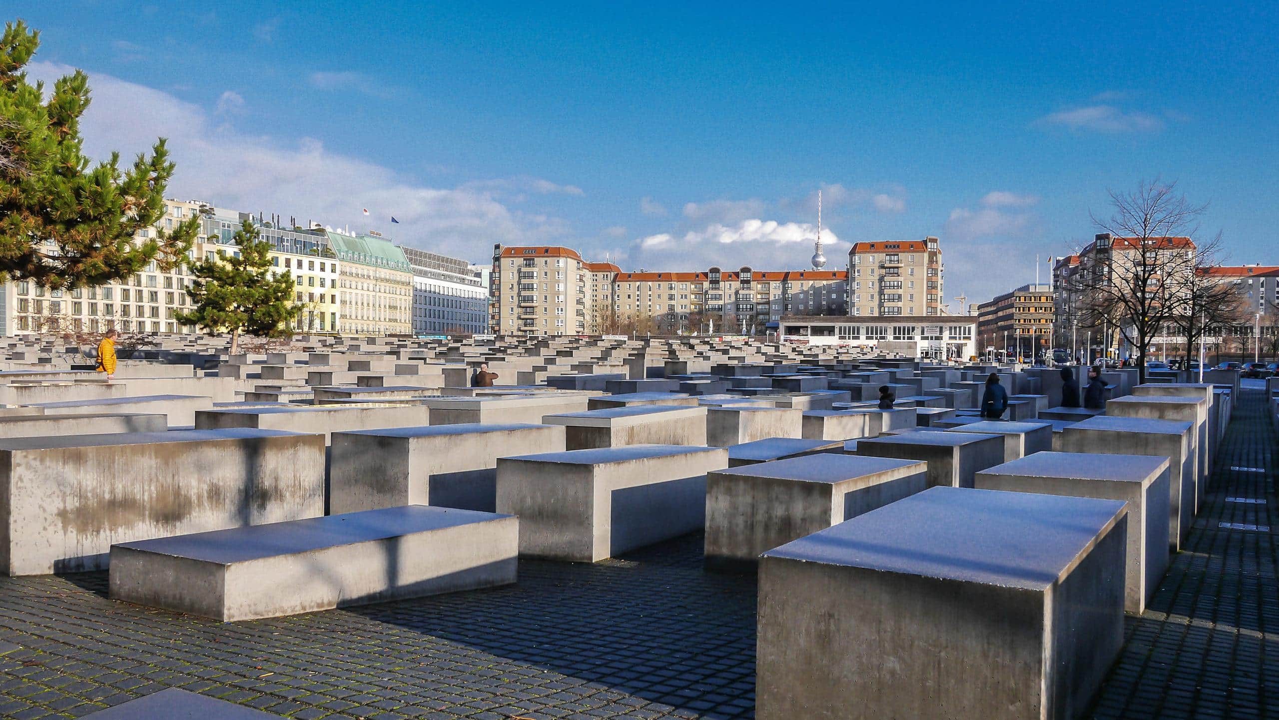 Památník holocaustu, Berlín. Betonové stély a budovy v pozadí. Turistická atrakce, vzpomínka na oběti.