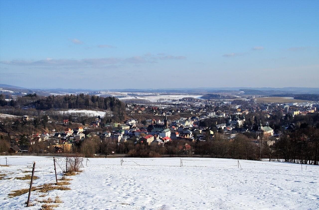 Zimní pohled na město, sníh, lesy a modré nebe. Krajina s architekturou a přírodou.