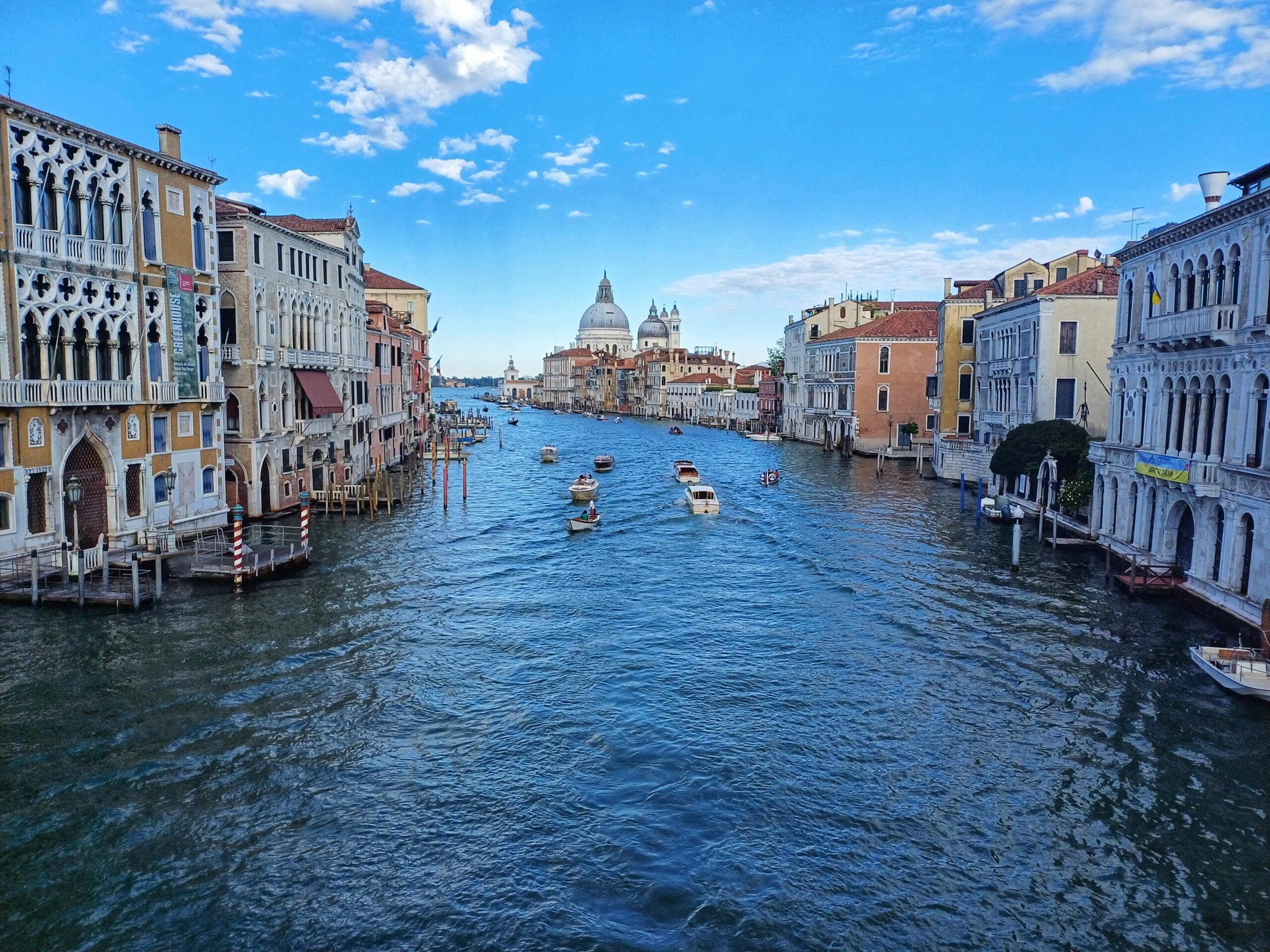 Benátky, Canal Grande s loděmi a historickými budovami. Italská architektura a modrá obloha.
