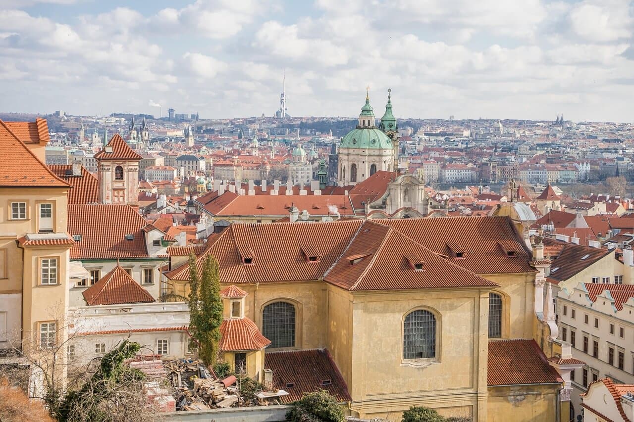 Panorama Prahy: červené střechy, kostely a věže. Nejužší ulička v Praze.