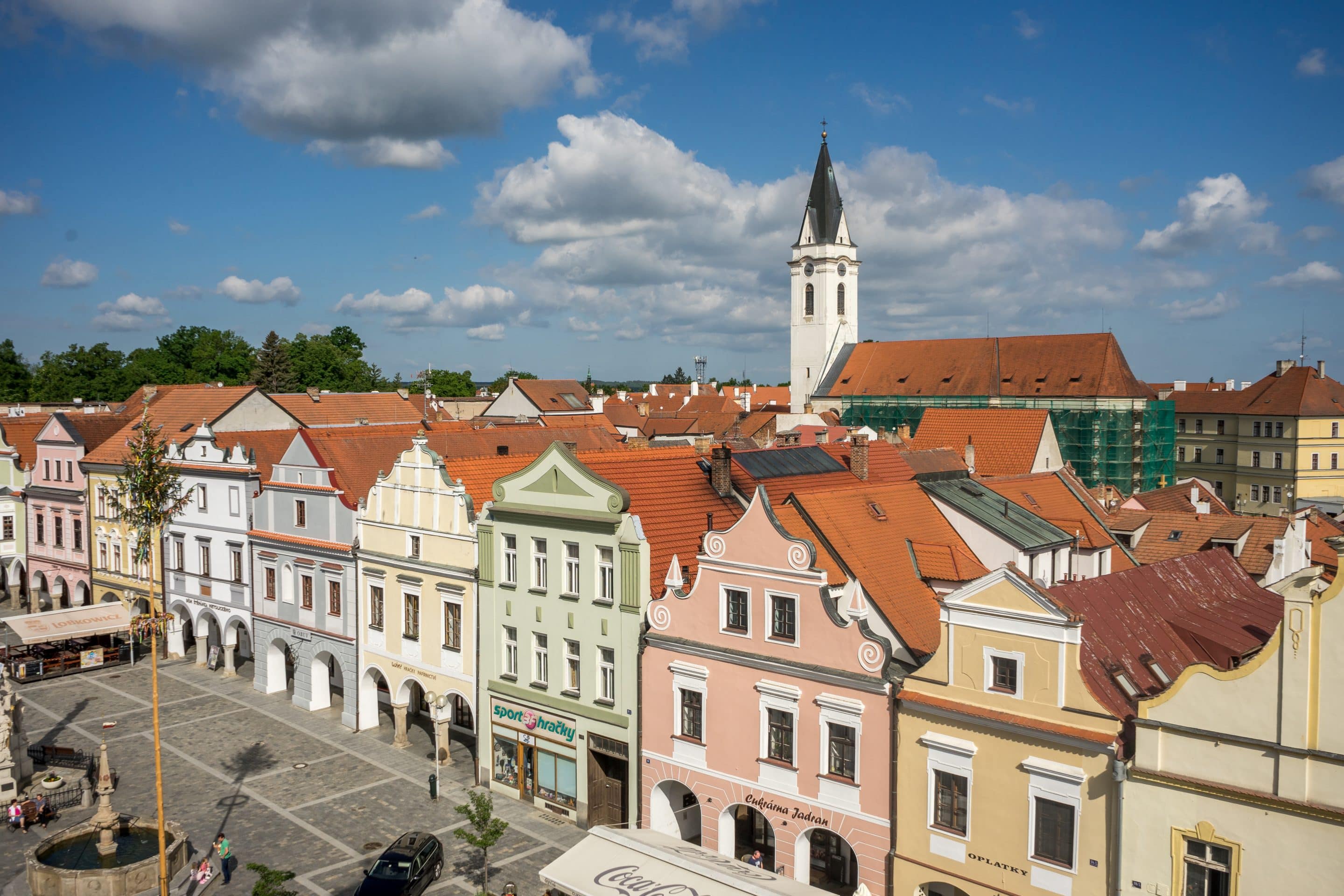 Třeboň, Česká republika: historické náměstí s barevnými domy, kostel a modrá obloha s mraky. Turistická destinace, památky UNESCO.