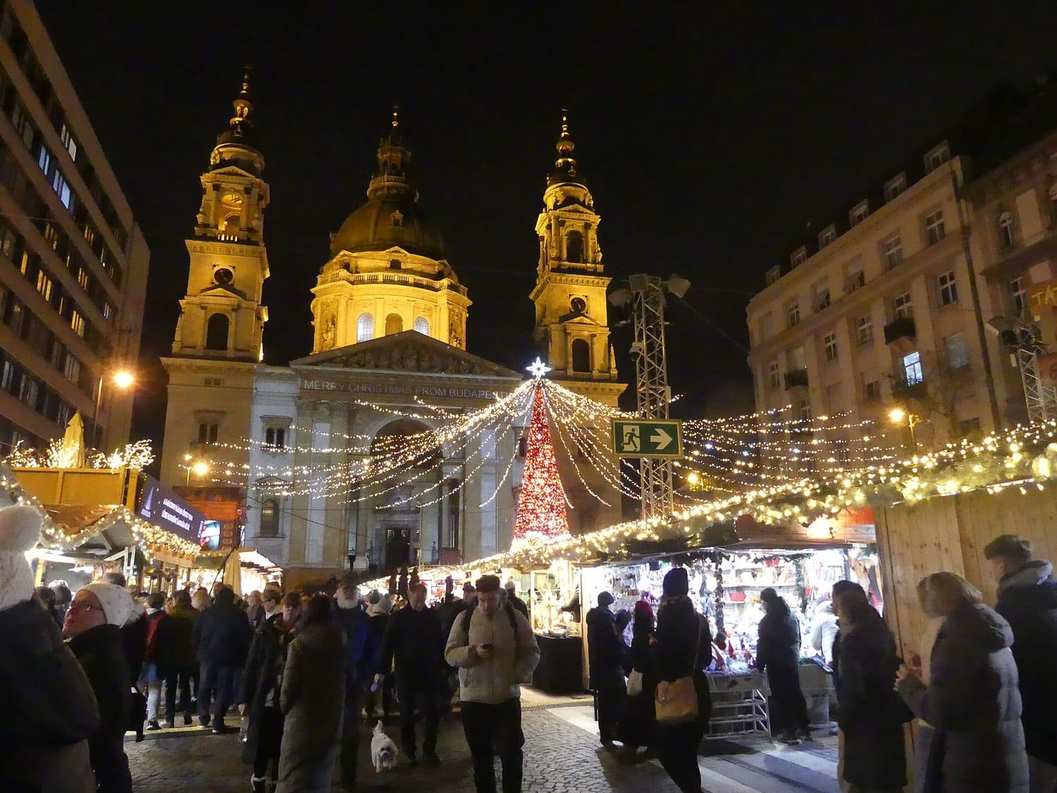 Vánoční trh u baziliky svatého Štěpána v Budapešti večer, stánky, osvětlený strom a lidé v zimním oblečení