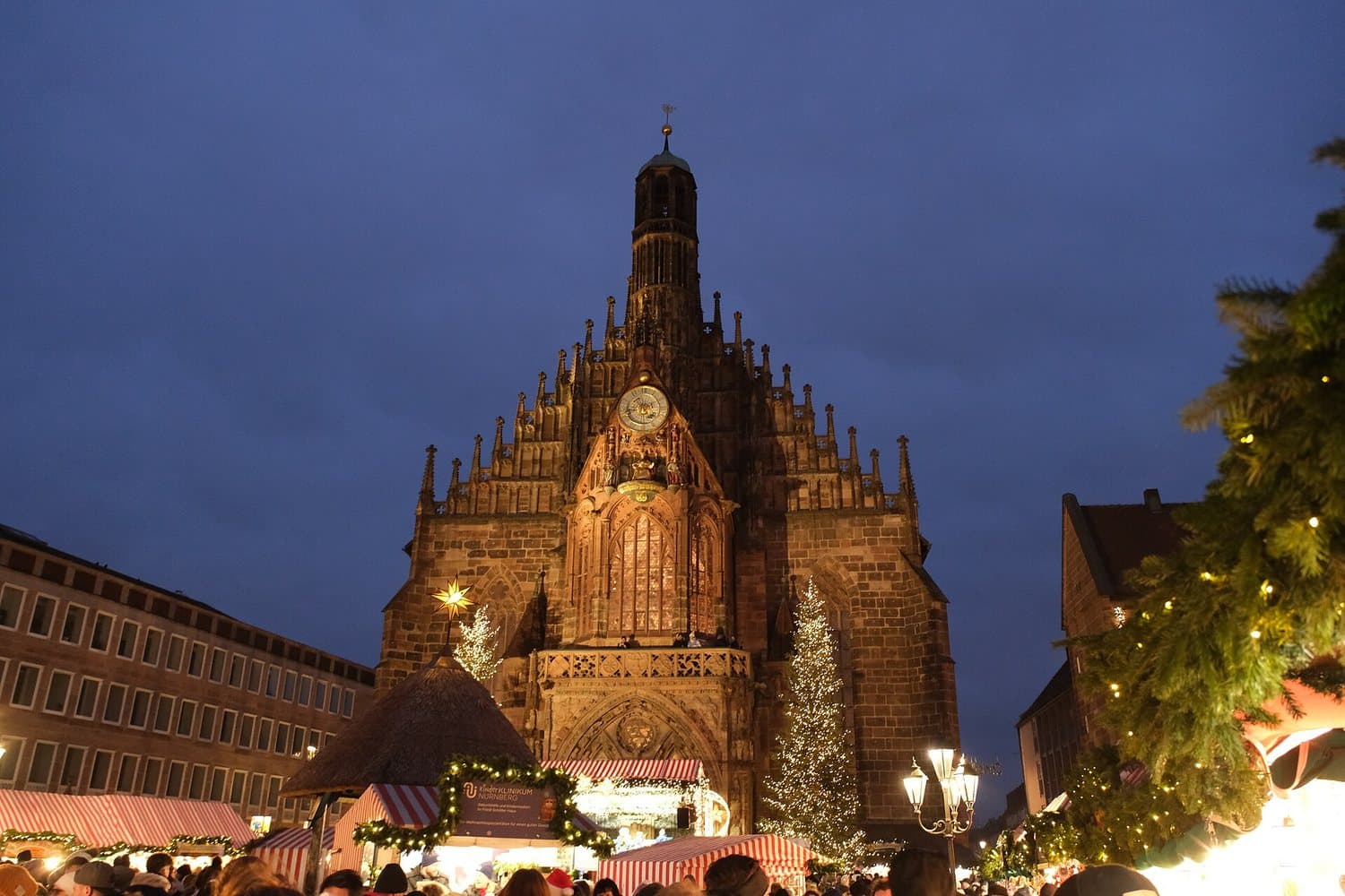 Kostel Frauenkirche za soumraku, před ním osvětlený vánoční strom a stánky Christkindlesmarktu v Norimberku