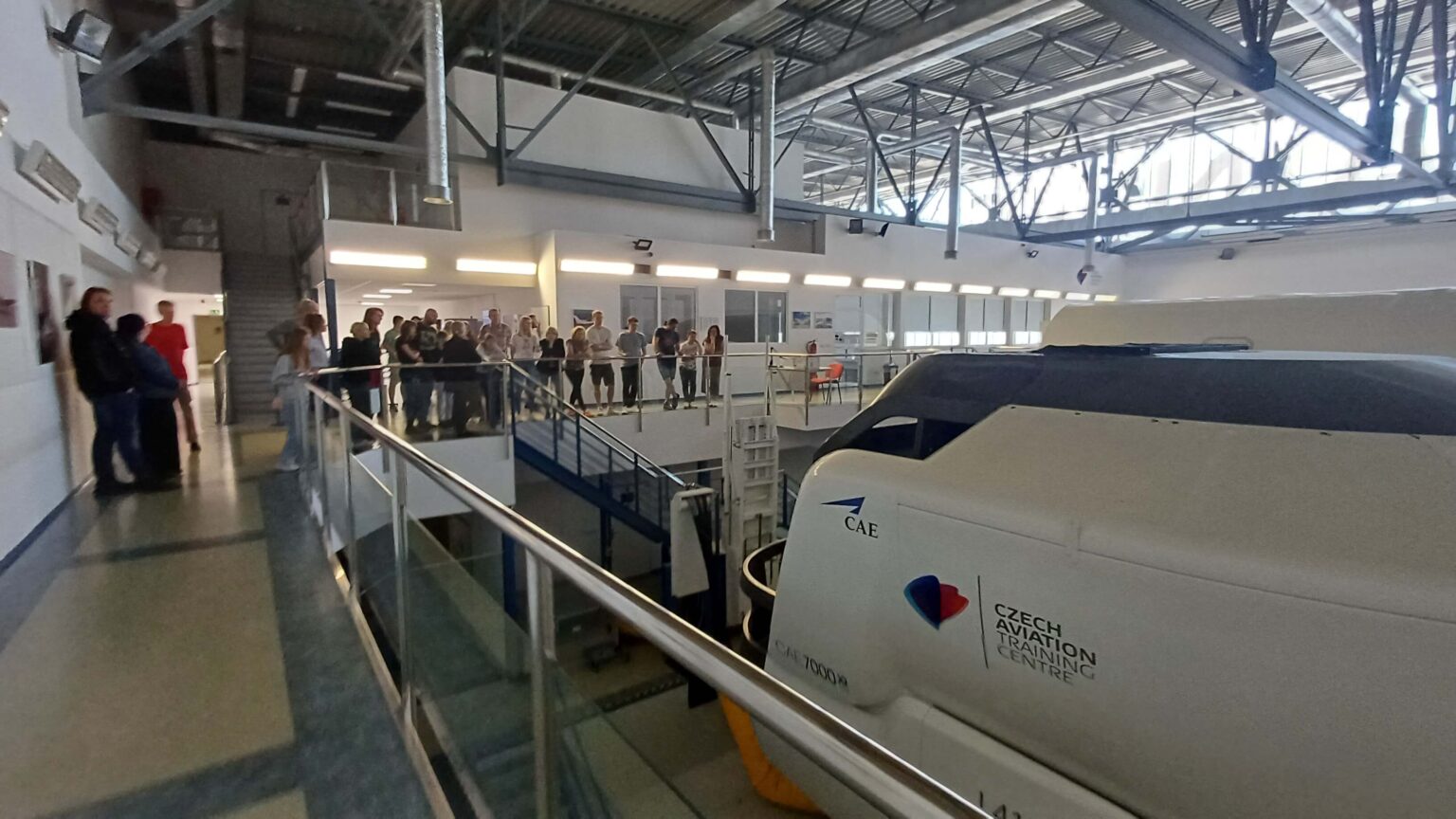 Hala výcvikového centra CATC se simulátorem CAE a skupinou návštěvníků na galerii