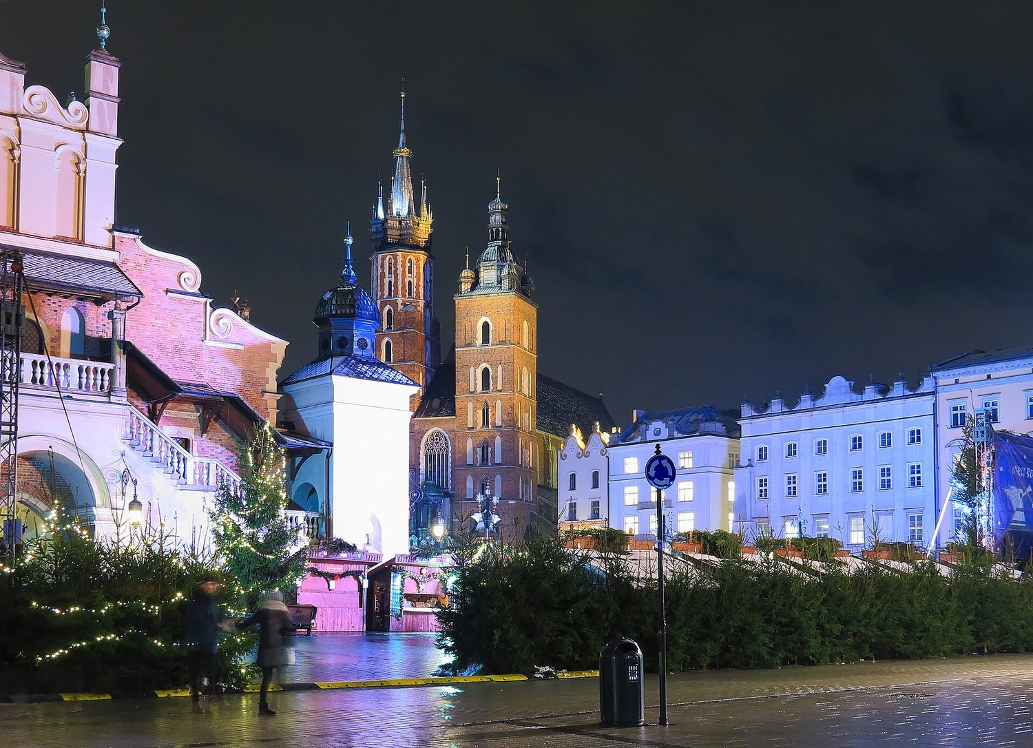 Mariánský kostel a Sukiennice v Krakově večer, v popředí stromky vánočního trhu