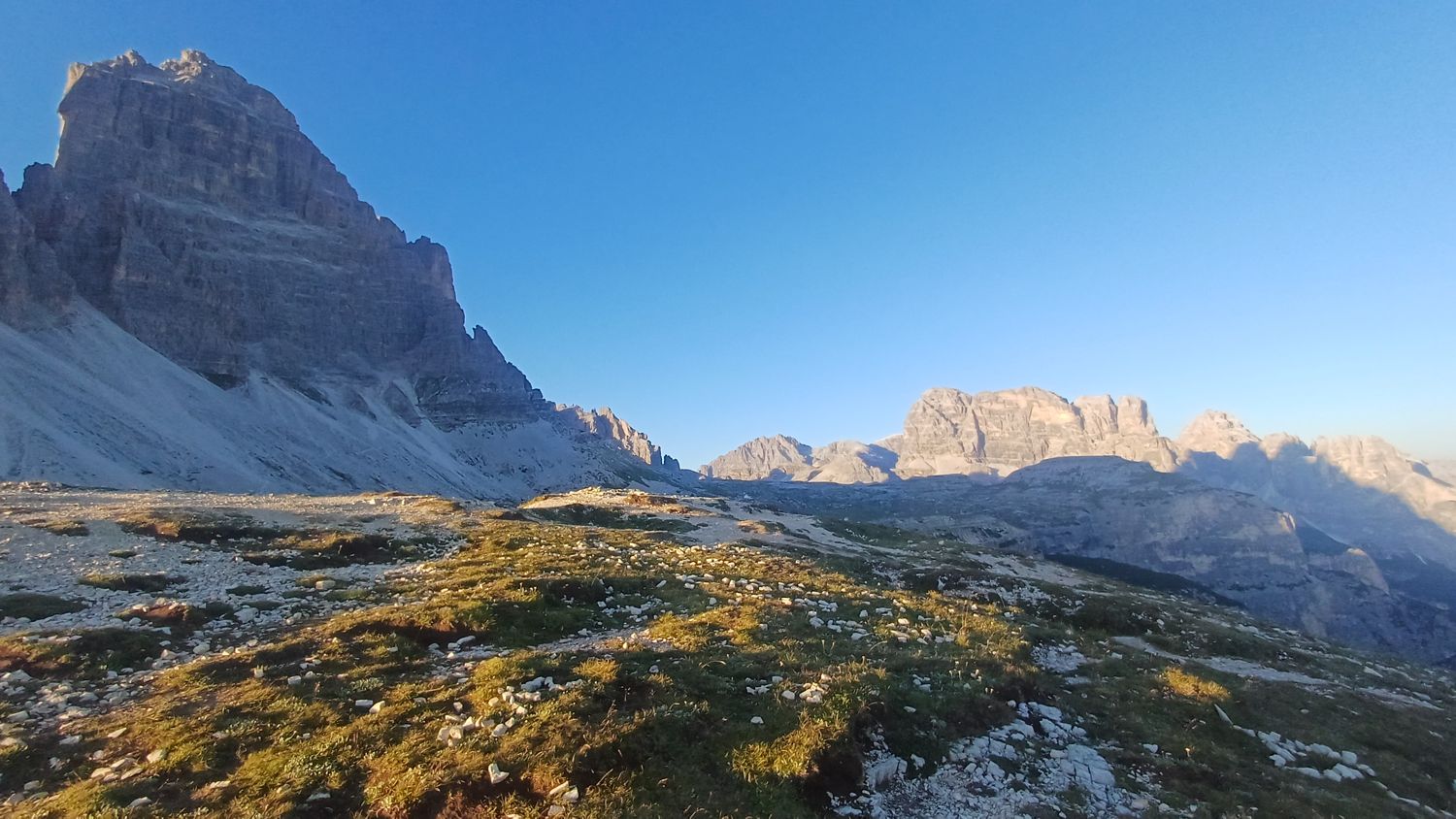 Masiv Tre Cime ve stínu a vzdálené štíty ve večerním světle