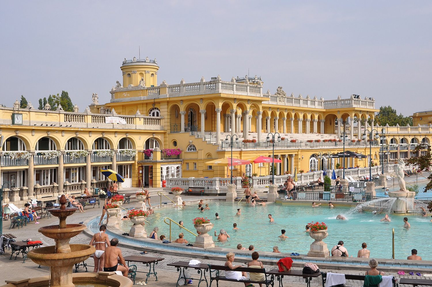 Venkovní bazény lázní Széchenyi v Budapešti, za nimi žlutá secesní budova a koupající se lidé
