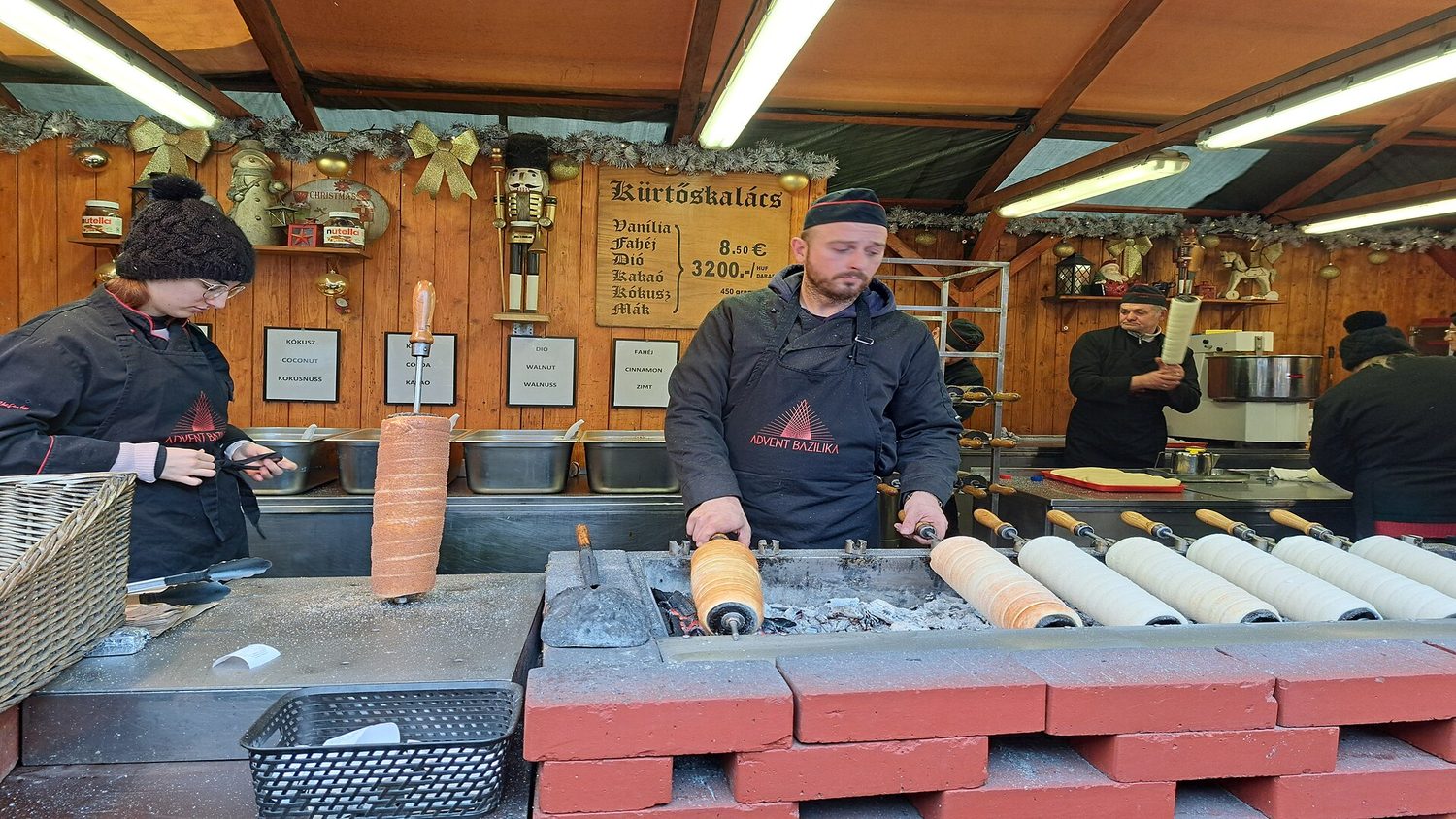 Kuchaři pečou kürtőskalács nad žhavým uhlím ve stánku na vánočním trhu u baziliky svatého Štěpána v Budapešti