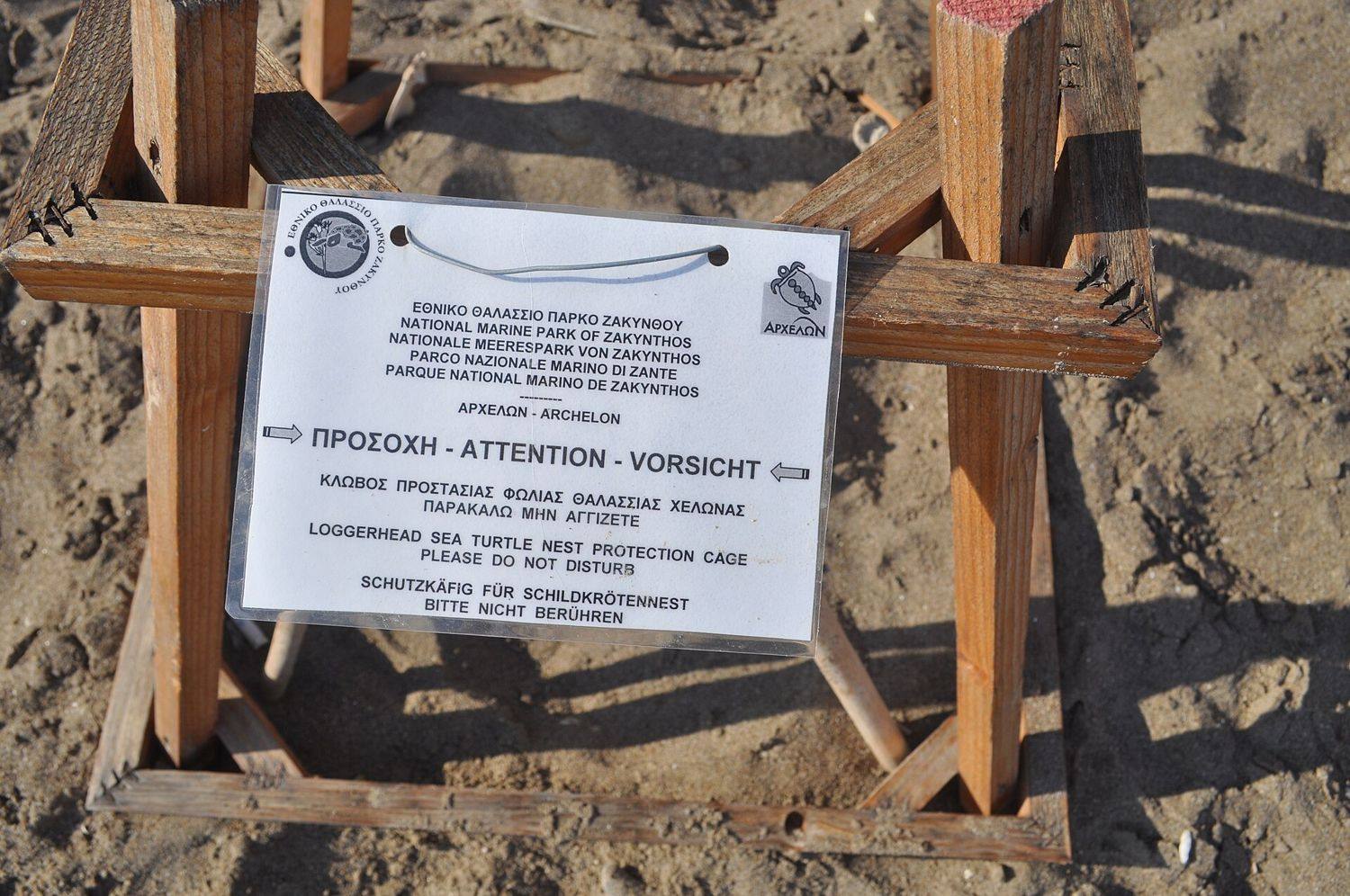Dřevěná klec nad želvím hnízdem na pláži Kalamaki s cedulí národního mořského parku